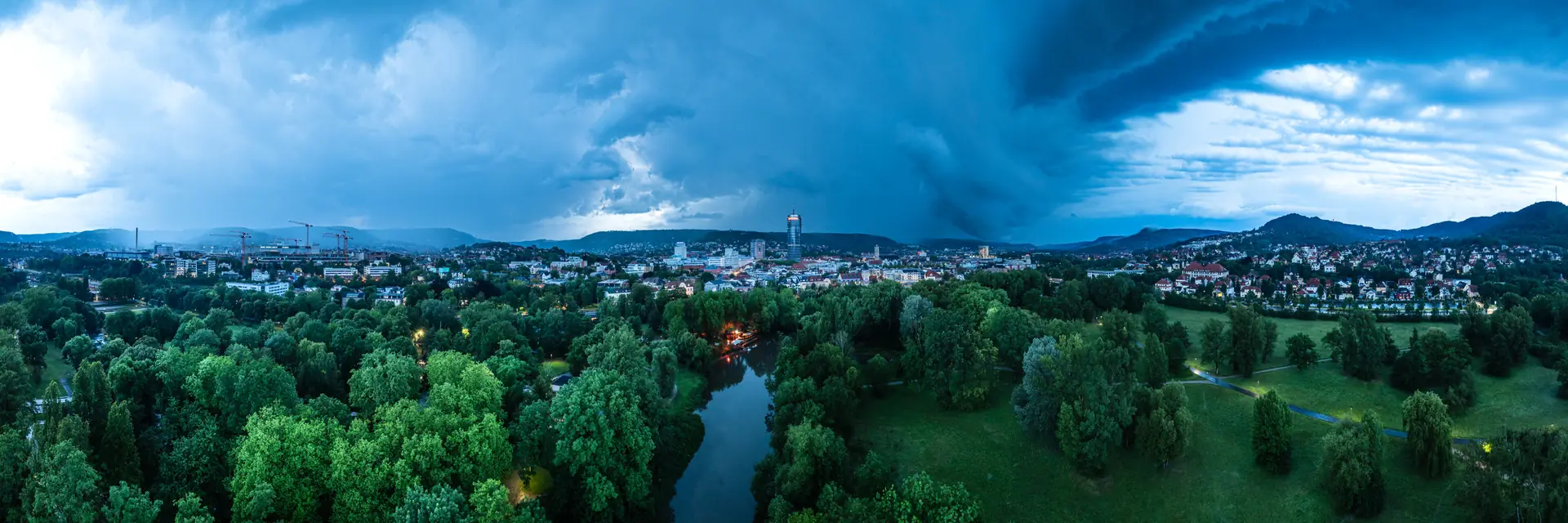 Dunkle Gewitterwolken über Jena und der Saale, darunter grüne Auenlandschaft