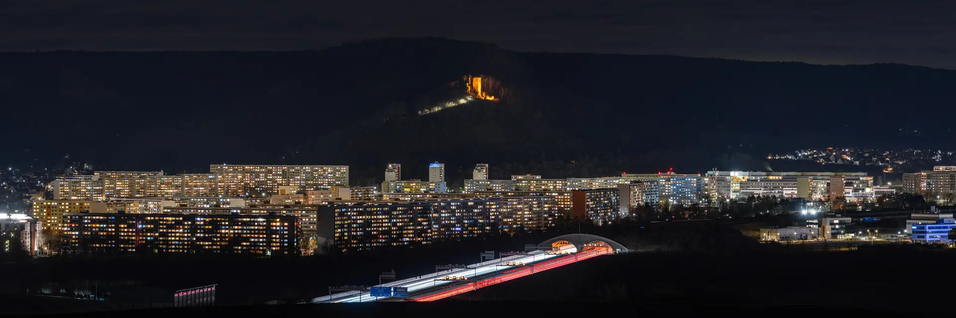 Jena bei Nacht, beleuchtete Wohnblöcke und Lichtspuren der Autobahn im Saaletal