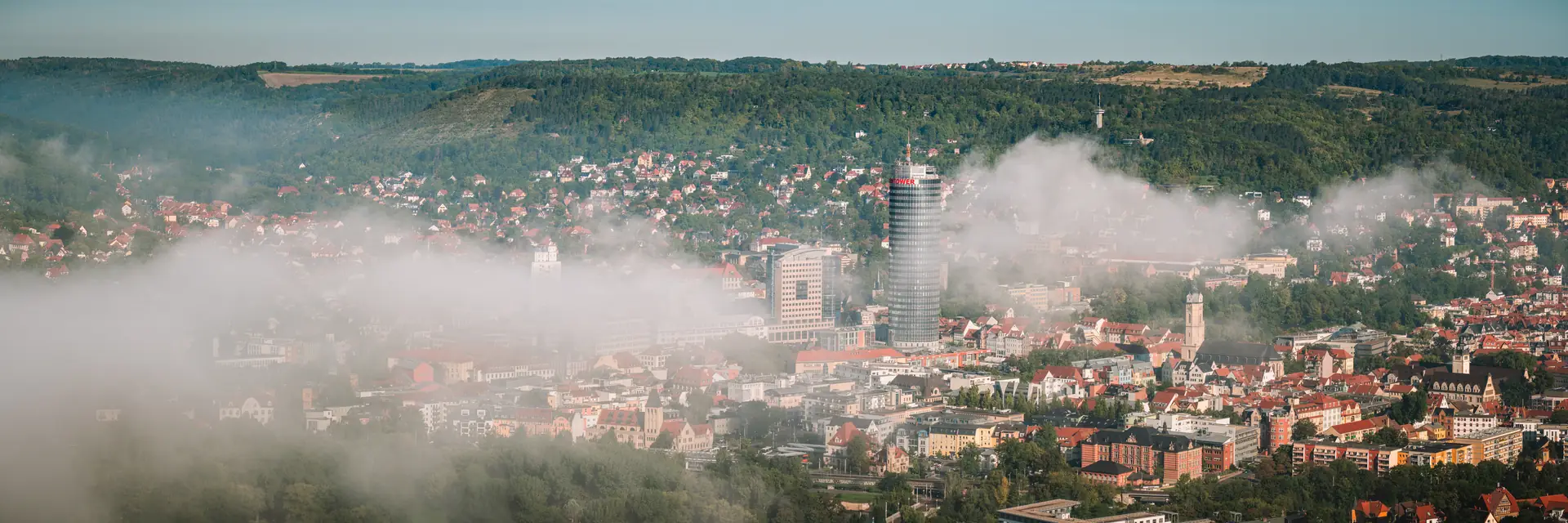 Jena unter einer Nebeldecke, der JenTower ragt aus dem Dunst über den Kernbergen